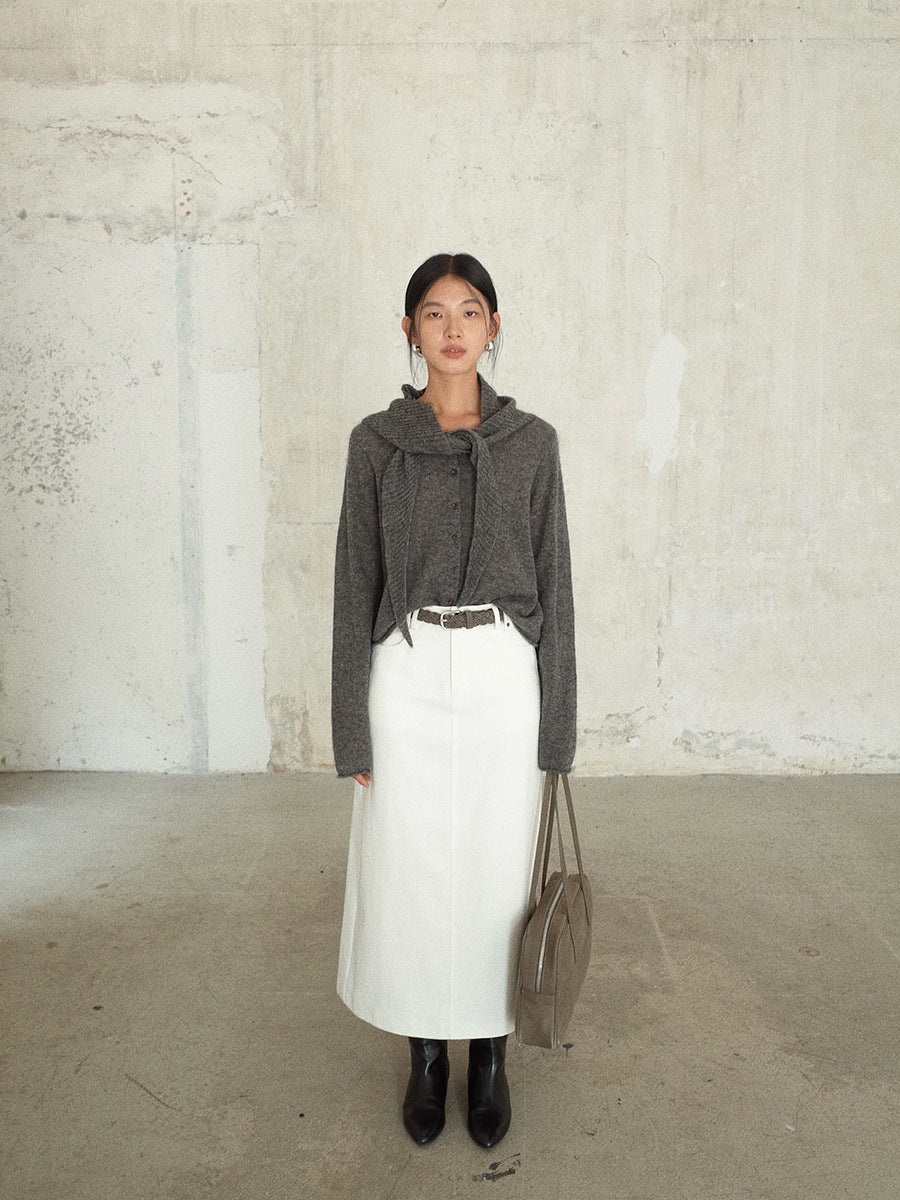 Woman wearing a gray cropped sweater, white High-waisted A-line Maxi Skirt , black boots, and holding a beige handbag against a plain background.
