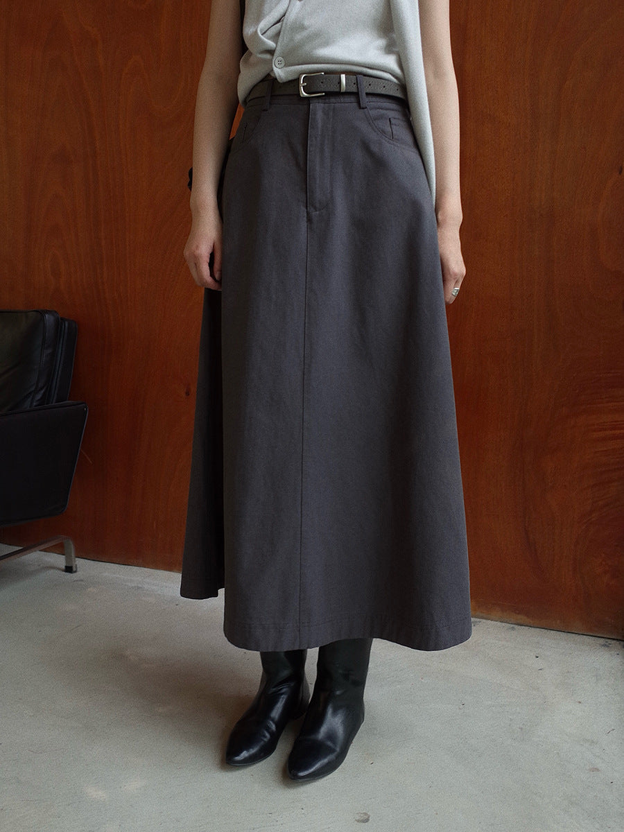 Person wearing a long dark gray Maxi Length A-Line Denim Skirt with a belt against a wooden wall.