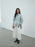 Woman wearing a light blue shirt, white Cropped Wide-Leg Straight Jeans, and dark shoes in a minimalistic setting.